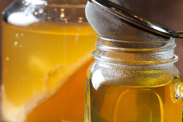 Kombucha tea in a glass Cup with a sieve for straining the drink and a jar with a mushroom in the...