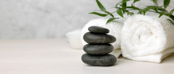 spa and wellness center - stack of massage stones and towels with green plant on white wooden table. banner copy space