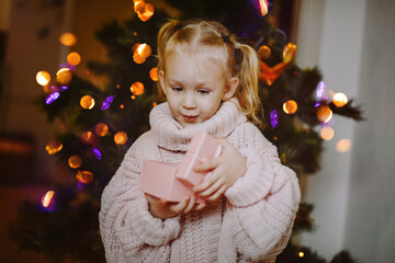 Little girl looking up with surprise and joy in open gift box on the background of the Christmas tree. Christmas tree on New Year's Eve