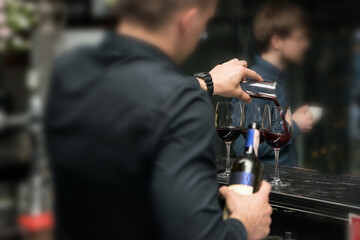 Barman pouring red wine into glasses in detail