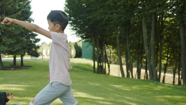 Little Asian boy in the park trains, kung fu, karate, kicks, stumbling, sunny summer sports