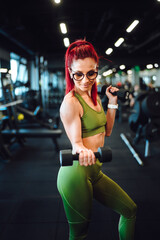 Female athlete exercising biceps in the gym, dumbbells.