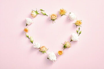 Heart symbol made of roses flowers and leaves on pastel pink background. Valentines day, mother day, anniversary celebration concept. Flat lay, top view.