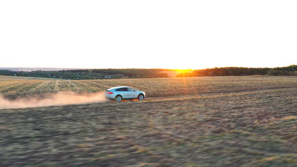Aerial shot of electrical car speeding through dusty route. Ecology friendly auto on electric charge driving along rural road with sunset landscape at background. Modern technologies concept