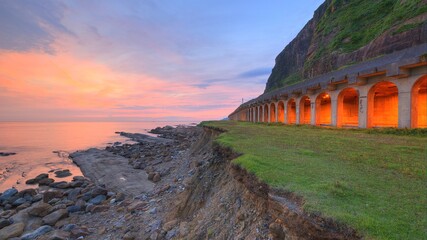 Sunrise scenery at a rocky beach with a coastal highway along the beautiful coastline under dramatic dawning sky ~ Scenic view of a rock shed tunnel at dawn on northern coast of Taipei, Taiwan