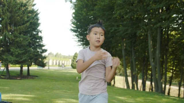 Little asian boy in the park trains, kung fu, karate, kicks, stumbling, sunny summer sports in the background