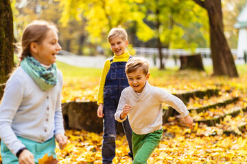 Three hyperactive kids running around each other and laughing. Group of children playing in autumn park.