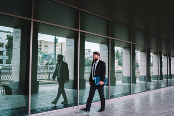 Fototapeta na wymiar Positive businessman walking along glass wall