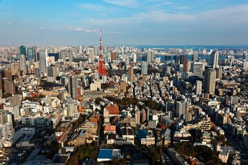 Fototapeta premium An aerial panorama from Roppongi over Downtown Tokyo, with landmark Tokyo Tower among crowded buildings, city streets crisscrossing the district & Tokyo Bay on distant horizon on a beautiful sunny day