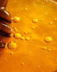 Wooden honey dipper with golden honey and air bubbles. Extreme close up