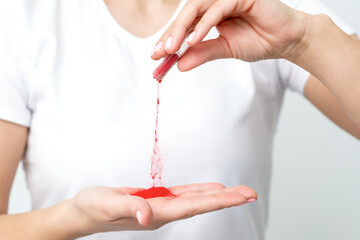 Closeup of manicure master pours red pigment nail powder from tube on her palm