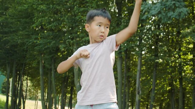 Little asian boy in the park trains, kung fu, karate, kicks, wall fight, sunny summer sports in the background
