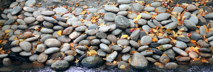 Large stones are laid in a line. Yellow leaves fall on the rocks. The fall of the year.