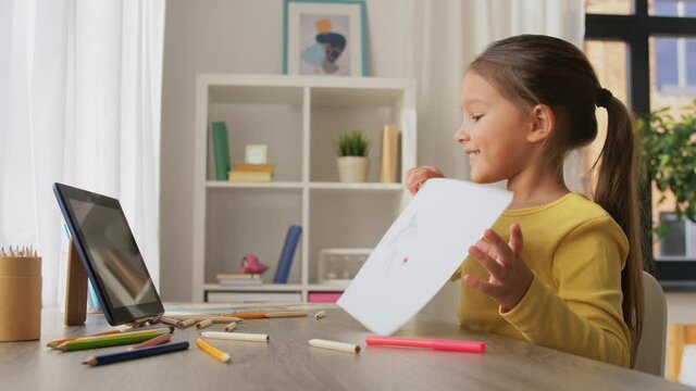 childhood, creativity and technology concept - happy smiling little girl having video call on tablet pc computer and showing her drawing at home