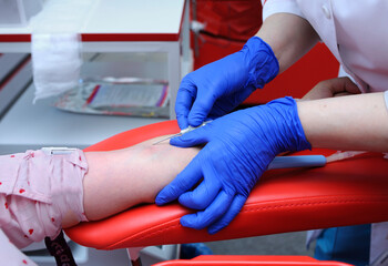 Nurse hands taking blood from the vain of a donor - hypodermic needle, tubes, container with blood