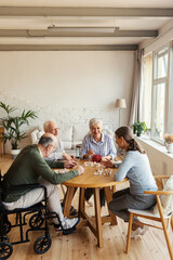 Group of four friendly senior people, two men and two women, sitting at table and enjoying playing...