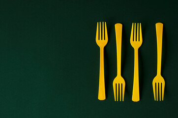 Plastic yellow forks on green paper background.