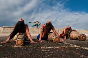 Girls dressed in different colors with their faces painted posing with drums sitting on their backs...