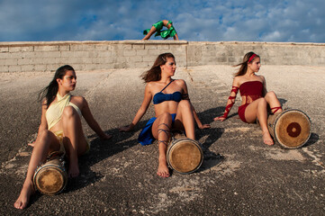 Girls dressed in different colors with their faces painted posing with drums sitting on a stone hill