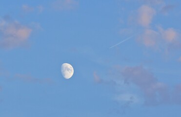 Luna gibbosa crescente in cielo parzialmente nuvoloso e la scia di un aeroplano