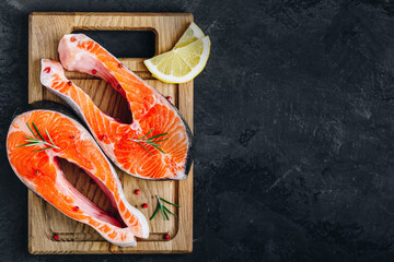 Fresh raw Salmon Steaks on wooden board prepared for cooking on dark stone background.