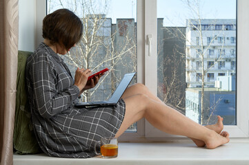 Attractive woman sit on windowsill with notebook and cup of tea