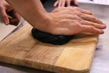Fototapeta na wymiar Male hands roll out the dough on a wooden board. The dough is black.