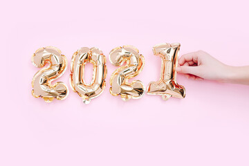 Female hand forming the number 2021, as the new year. New year celebration. Gold Air Balloons on pink background.