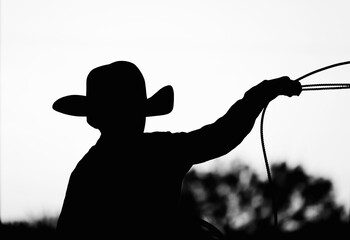 Young cowboy silhouette while roping for western rodeo lifestyle concept in black and white. - obrazy, fototapety, plakaty