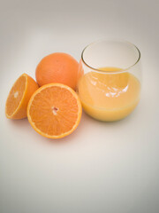 A glass goblet with orange juice. Juicy vibrant colorful oranges. Orange cut in half