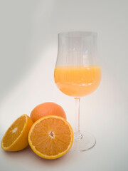 A glass goblet with orange juice. Juicy vibrant colorful oranges. Orange cut in half