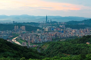 Aerial panorama of suburban residential communities in Taipei, with view of Taipei 101 Tower among skyscrapers in downtown, bridges over Xindian River & mountain silhouettes in the distant background