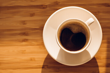 Cup of black coffee on bamboo desk in morning sunlight