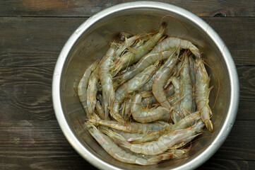 Fresh white tiger prawns in a metal cup on a wooden table. Fresh shrimp for cooking in the kitchen.