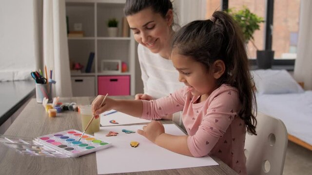family, motherhood and leisure concept - mother spending time with her little daughter painting wooden craftwork with brush and colors at home