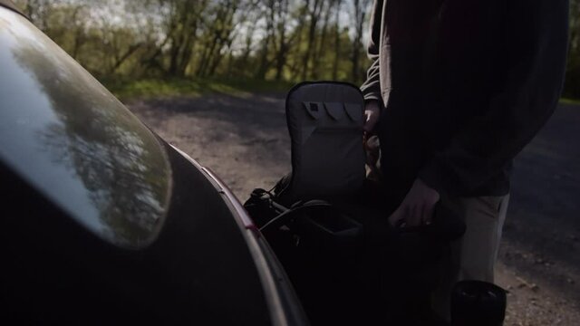 SLOW MOTION: Young Guy Packing his Backpack in Trunk of Car in Beautiful Summer Light 