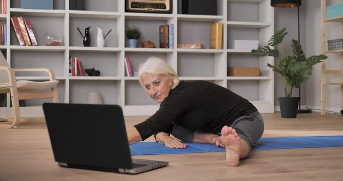 mature woman exercise work out at home online personal trainer,wellness healthy lifestyle elderly woman stretching yoga watching an online course on the computer