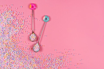 Pile of pastel color sugar balls with spoons on pink background with copyspace. Mixed colorful candies for sweets decoration. Rainbow colored sugar candies, dragee, confectionery. Sweets and desserts