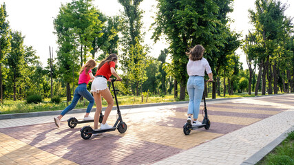 E-scooter, electric scooter, Ecological urban city transport, alternative energy, alternative lifestyle. Three Young girl friends on vacation having fun driving electric scooter through city park © irissca