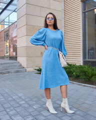 Elegant woman in blue dress walking city street. Pretty girl in white shoes
