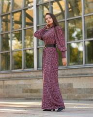 Elegant girl wearing purple dress and walking city street near glass modern wall