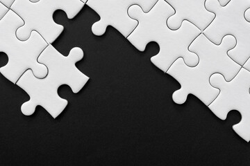 Obraz premium Unfinished white jigsaw puzzle pieces on black background with copy space