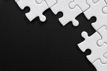 Fototapeta premium Unfinished white jigsaw puzzle pieces on black background with copy space