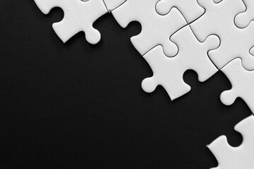 Obraz premium Unfinished white jigsaw puzzle pieces on black background with copy space