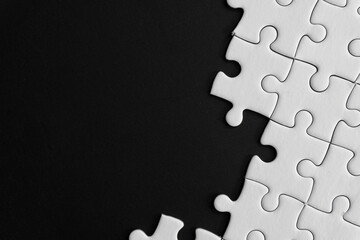 Unfinished white jigsaw puzzle pieces on black background with  copy space