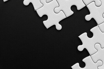 Unfinished white jigsaw puzzle pieces on black background with  copy space