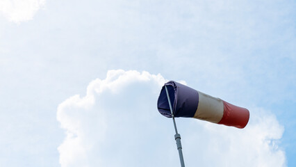 Flying windsock wind vane with red, white and blue lines on dramatic sky background. Test wind...