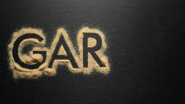 Writing word "Garlic" from dry garlic powder on black background. Stop motion.
