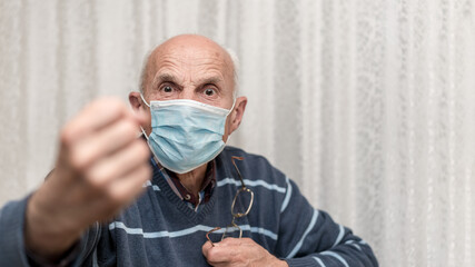 angry aggressive elderly man wearing face mask showing big fist self isolation and coronavirus...