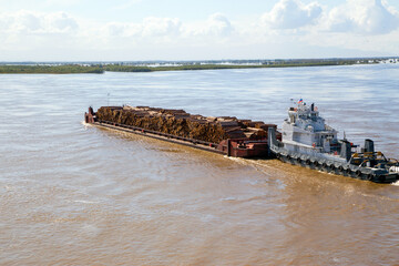The barge transports timber along the river. Horizontally.